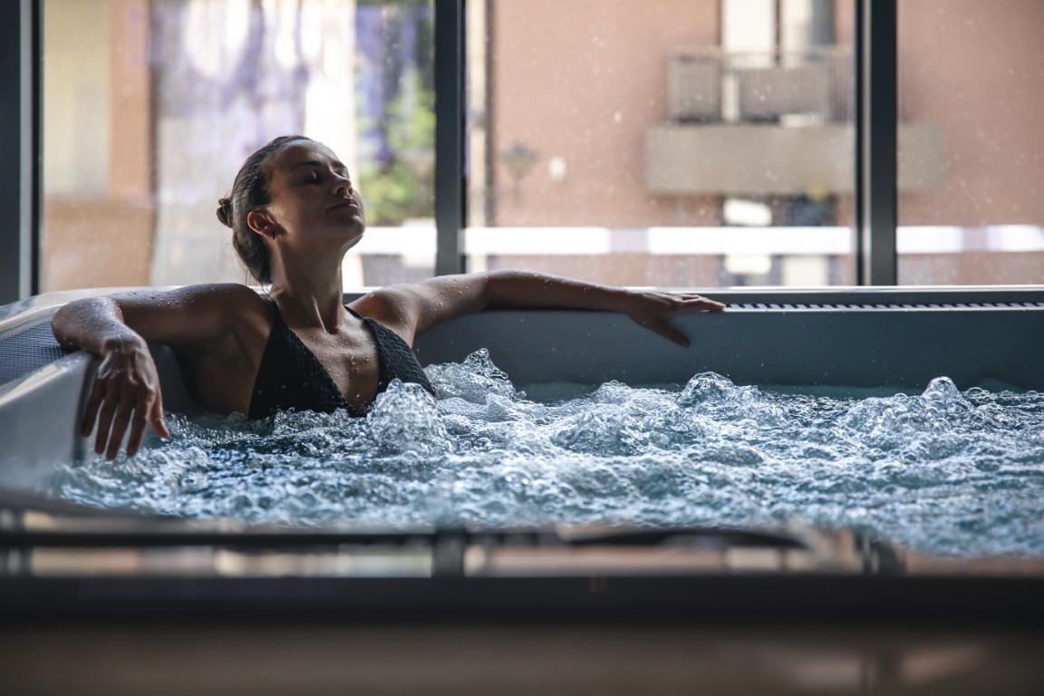 Attractive young woman in a black swimsuit is relaxing in a jacuzzi.